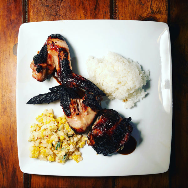 a plate of grilled chicken with corn salad and rice