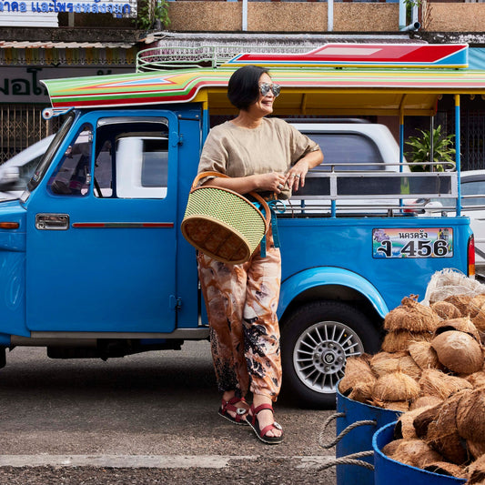 Nok Suntaranon standing next to a blue truck with coconuts in a market setting