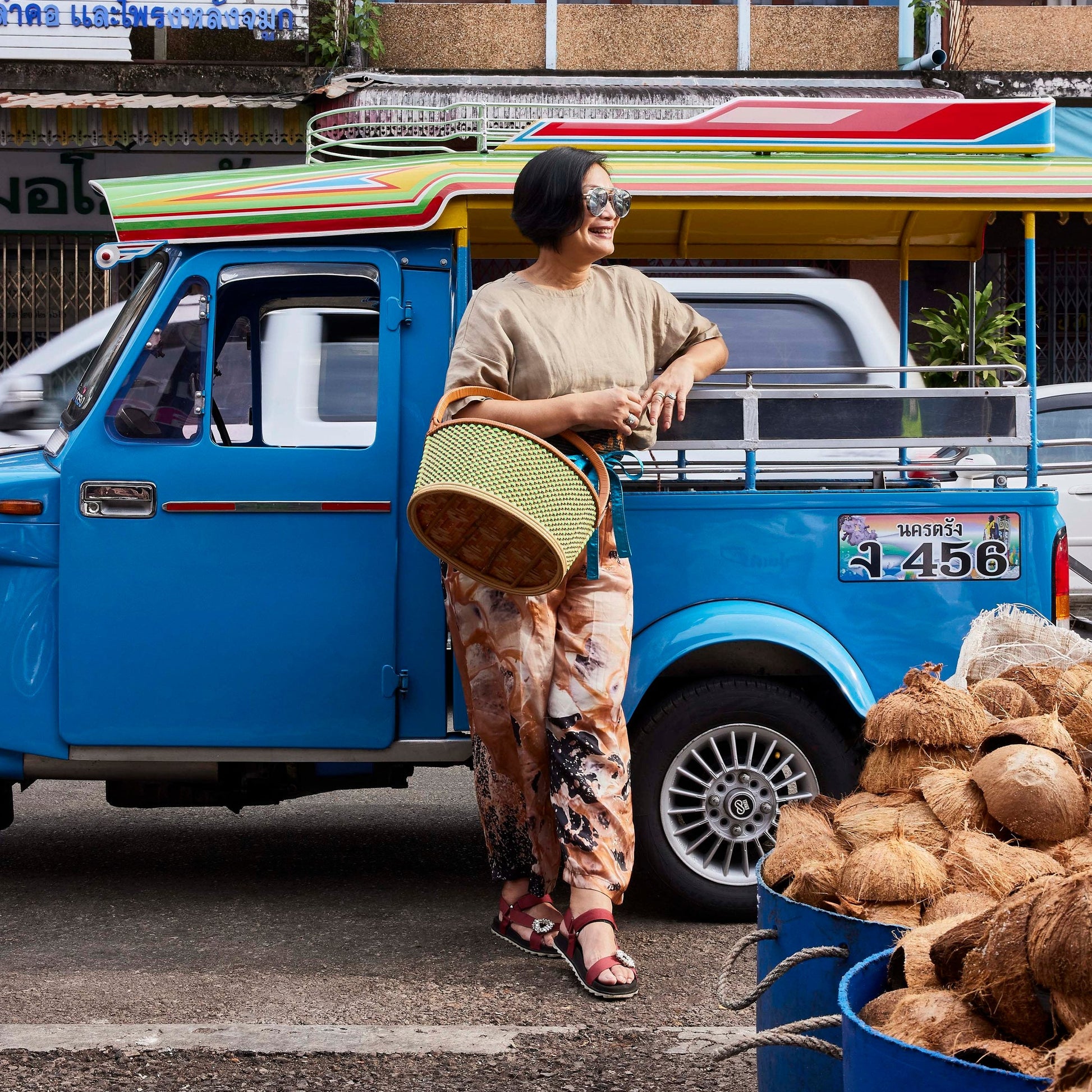 Nok Suntaranon standing next to a blue truck with coconuts in a market setting